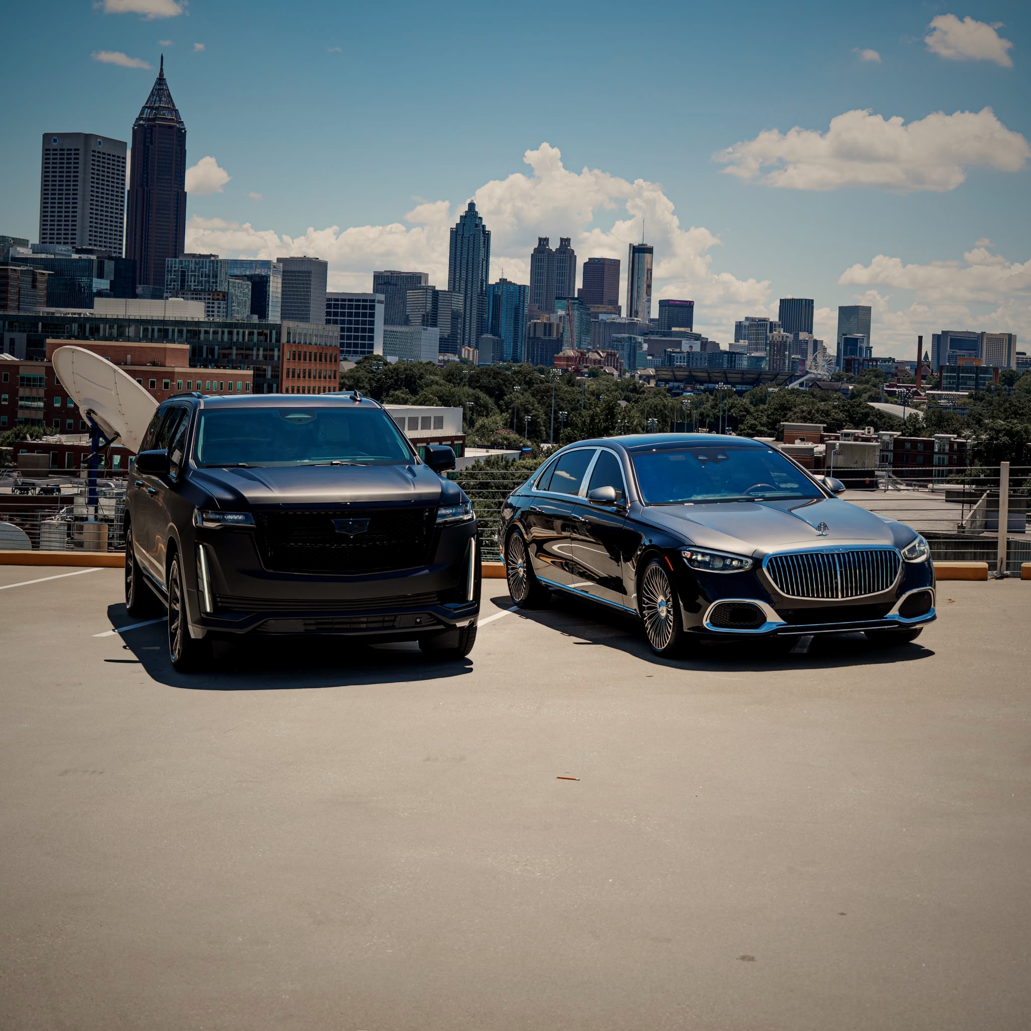 Black Cadillac Escalade and Mercedes-Maybach parked on a rooftop overlooking the Atlanta skyline